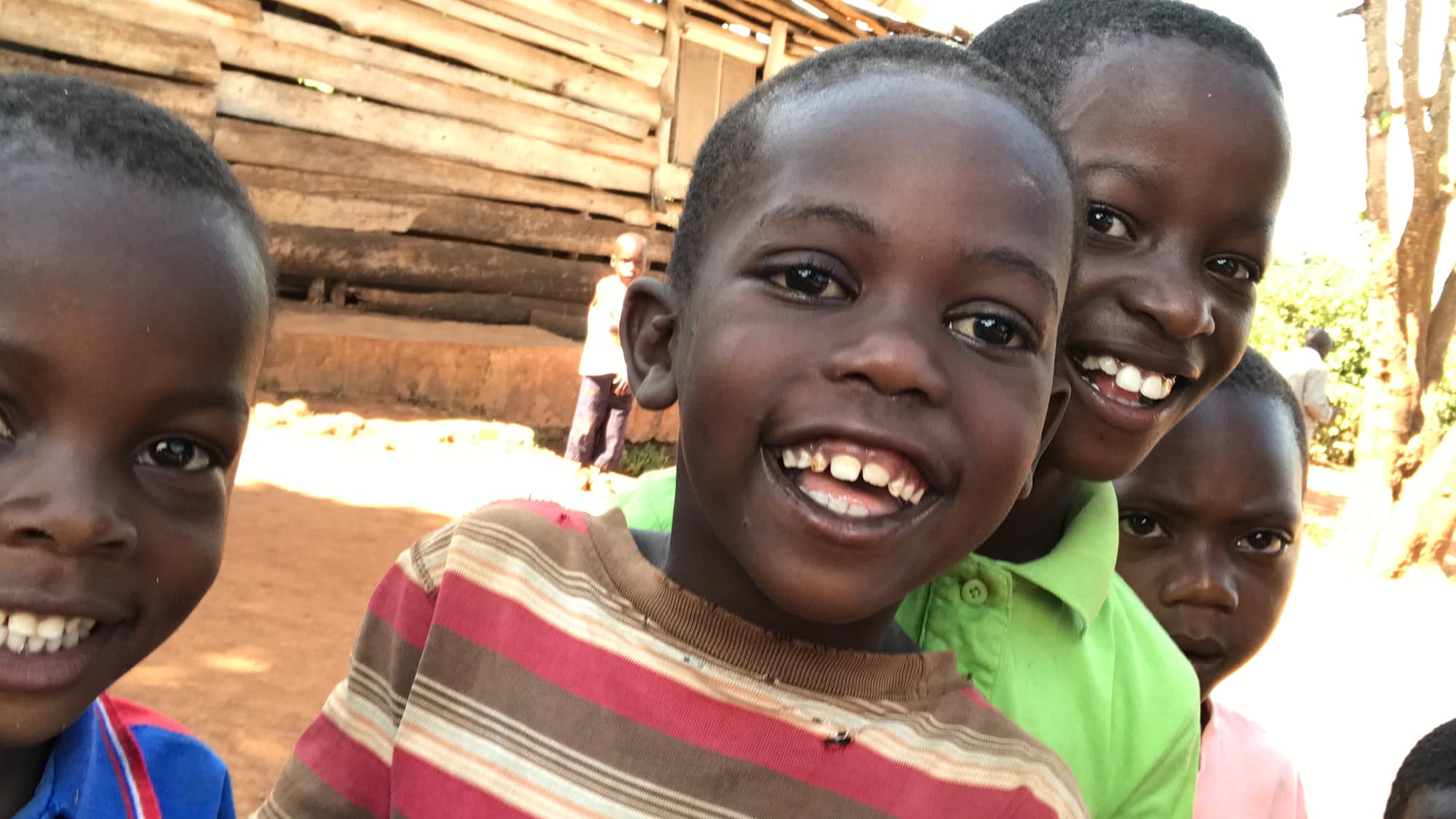 Children smiling outside a home in Uganda.